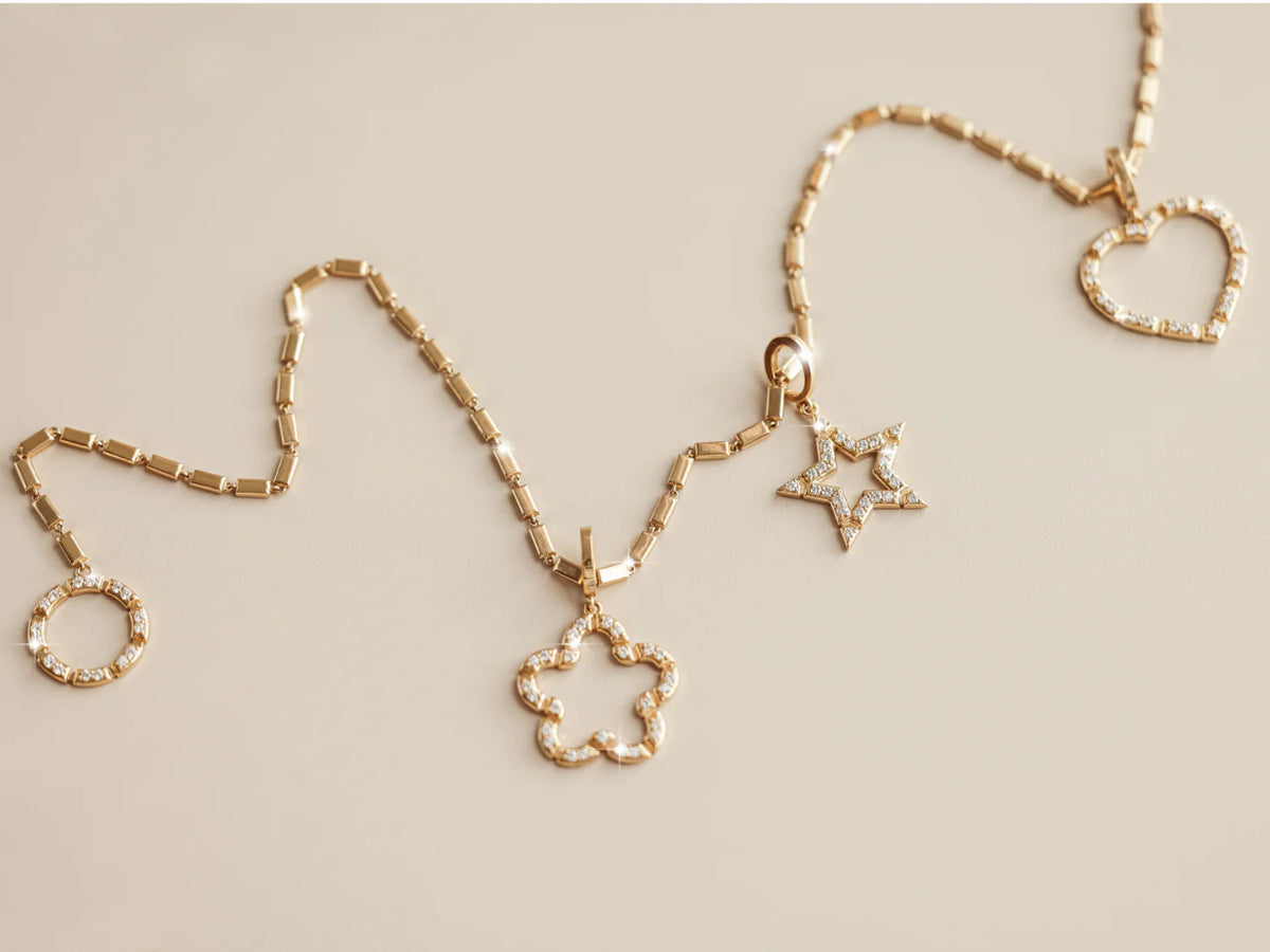 Onirikka Gold necklace with heart, circle, and star pendants on a beige background