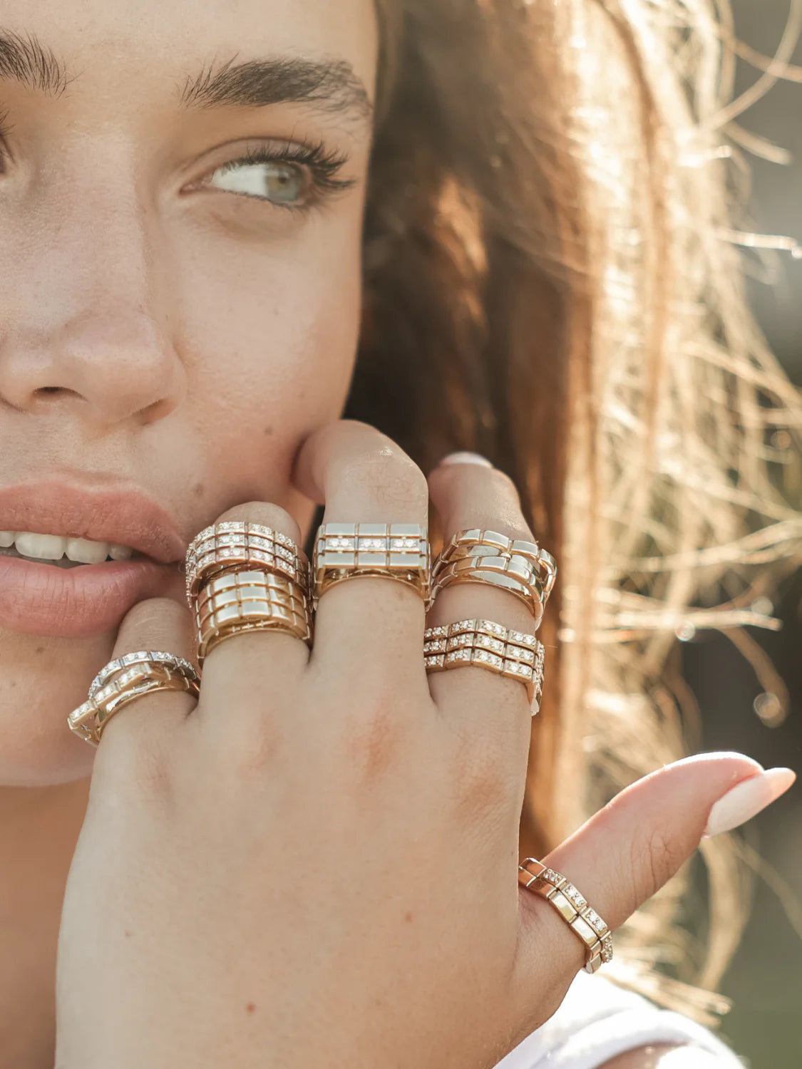 Woman wearing multiple Onirikka gold rings on a blurred natural background