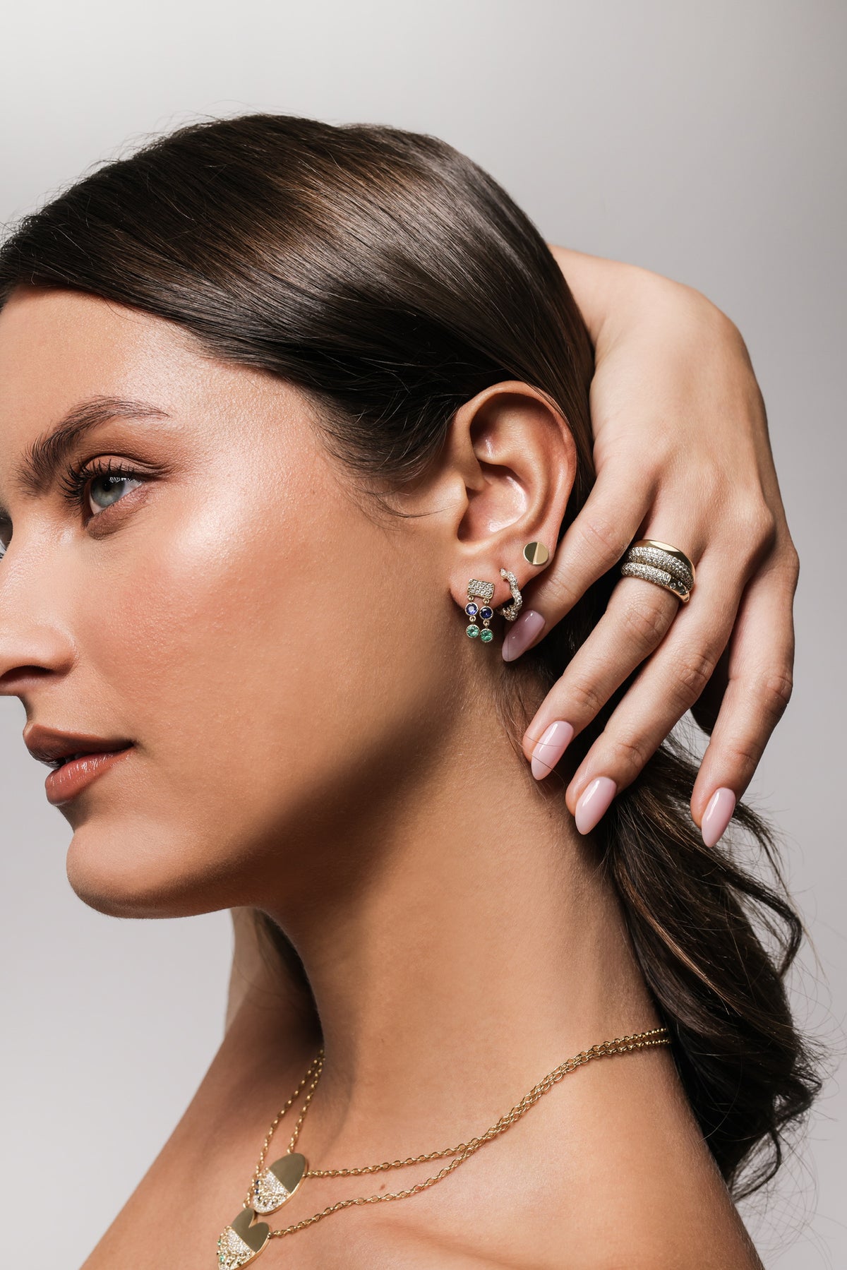 Close up of a Woman wearing Onirikka gold earrings and a ring, with a neutral background