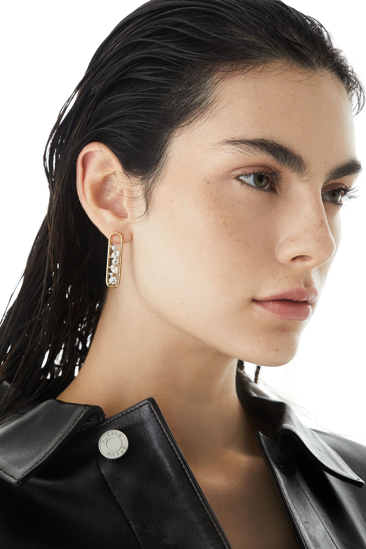 Close-up of a woman wearing a black leather jacket with a focus on her Rosario Navia Mara Drop Earrings in yellow gold and diamonds over a white background.
