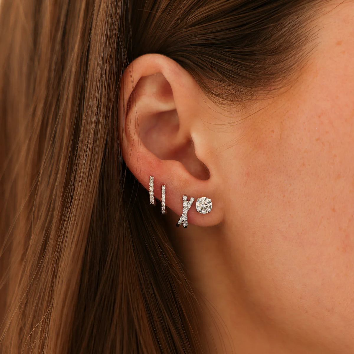 Dana Rebecca Designs Ava Bea Crossover Mini Huggie Earrings in white gold styled on models ear with a diamond stud earring and two diamond huggies