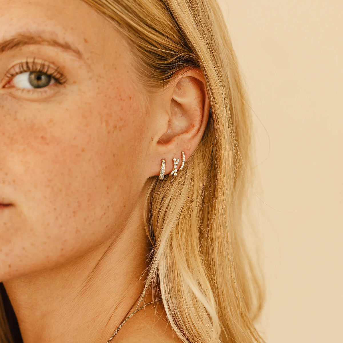 Dana Rebecca Designs Ava Bea Crossover Mini Huggie Earrings in yellow gold styled on models ear wearing two different kinds of diamond huggies