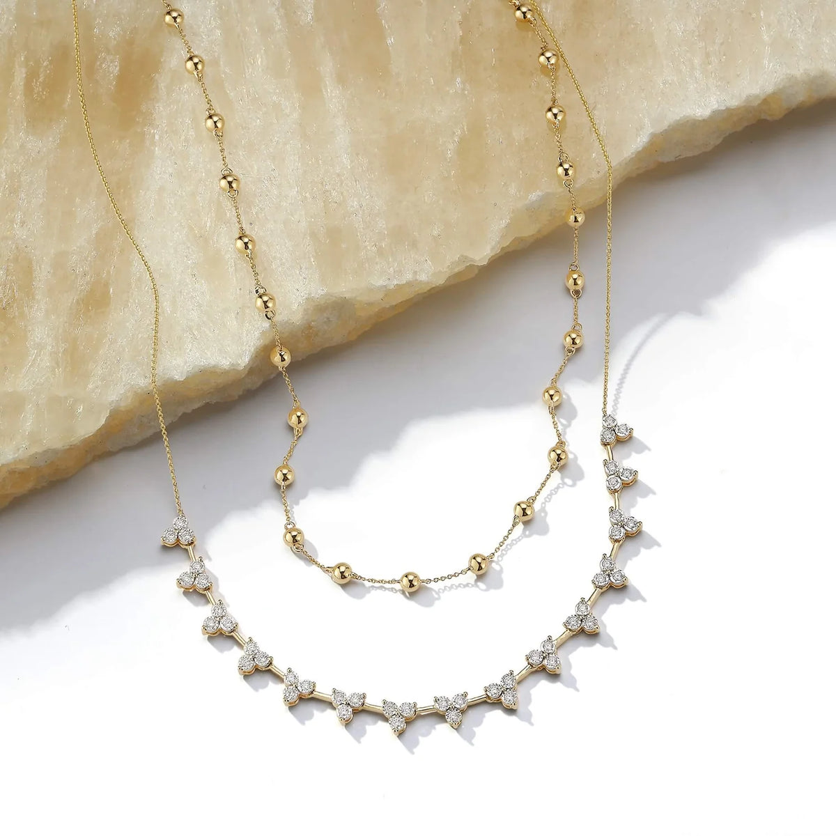 Dana Rebecca Designs Ava Bea Interval Trio Tennis Necklace in yellow gold styled on white surface with pebble station necklace