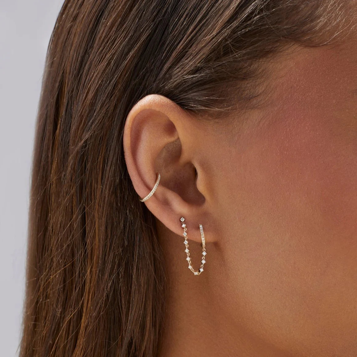 Close up of EF-Collection Diamond Mini Huggie & Prong Set Chain Stud Earrings in yellow gold on models ear with diamond cuff