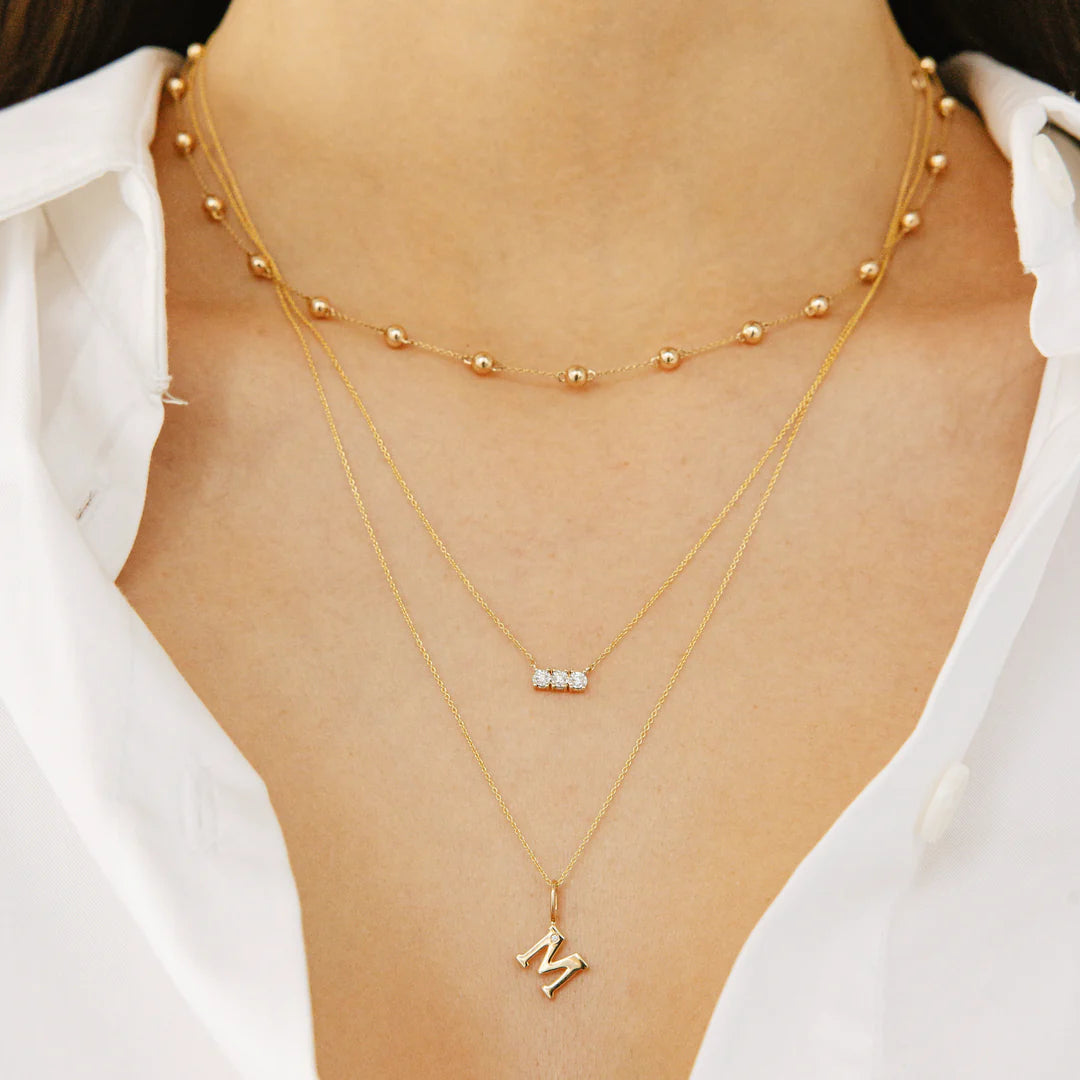 Dana Rebecca Designs DRD Gold Initial Charm in yellow gold on models neck wearing a white shirt