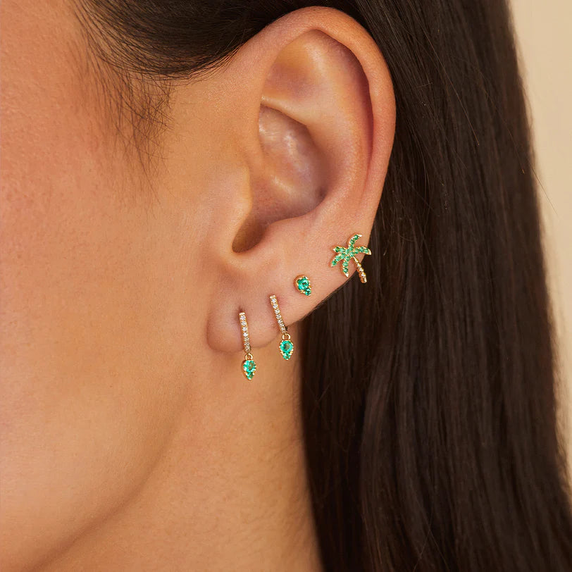 EF Collection Emerald Teardrop Diamond Mini Huggie Earring in yellow layered with emerald stud on models ear.