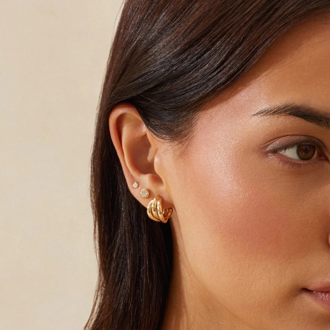 Close-up of a woman wearing Ef Collection Gold Knot Huggie gearrings with a neutral background.
