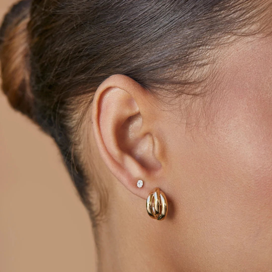 Close-up of an ear wearing Ef Collection Gold Knot Huggie earrings with a blurred background