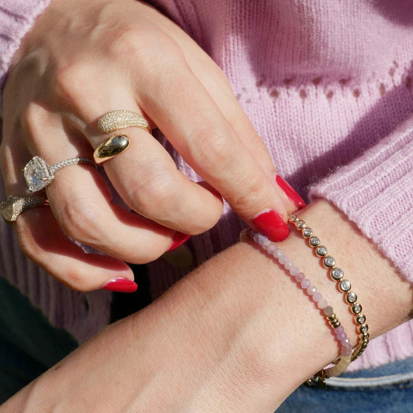 Product shot of EF-Collection Graduated Diamond Pillow Tennis Bracelet in yellow gold styled on models wrist with pink bead birthstone bracelet