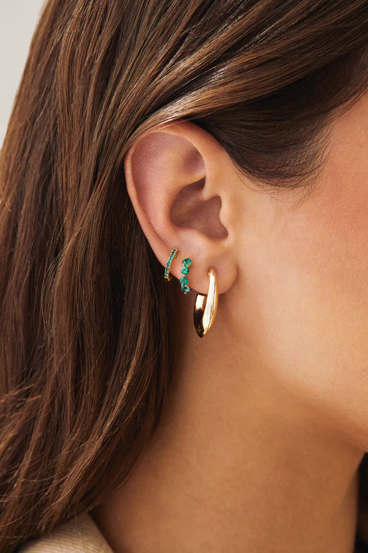 Ef collection Single Jumbo Prong Set Emerald Mini Huggie Earrings in yellow gold on models ear styled with different hoops.
