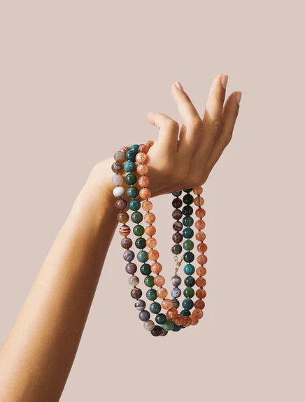 Hand holding three multicolored beaded bracelets against a beige background