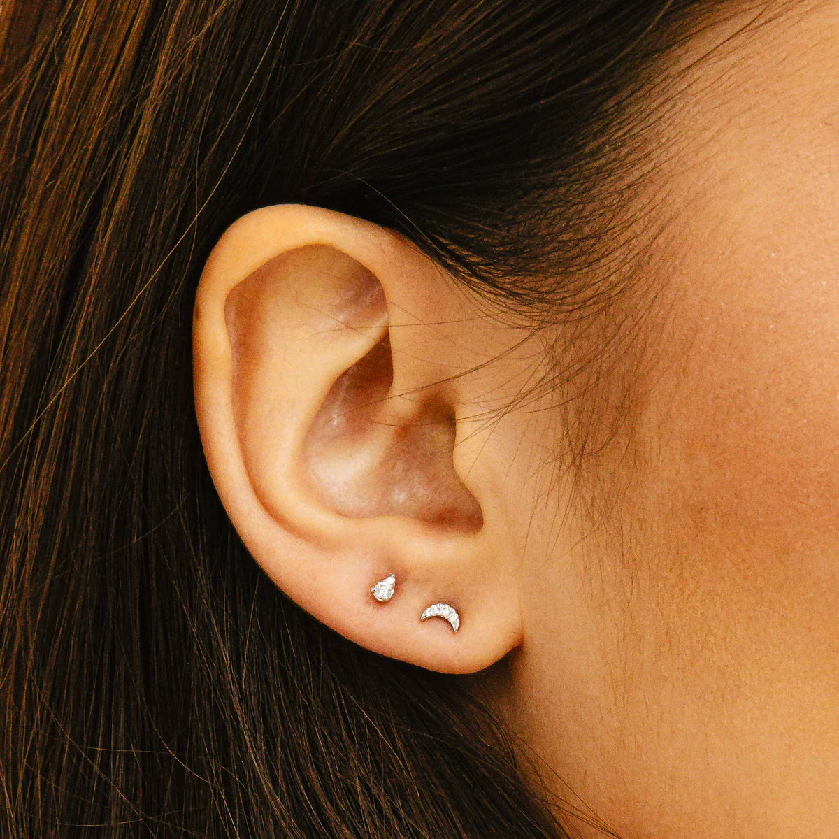close up of Dana Rebecca Designs mini crescent moon stud earrings in white gold styled with other studs