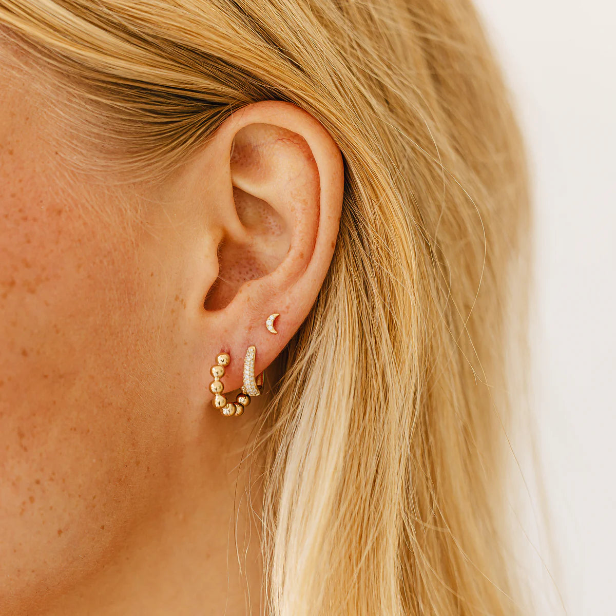 close up of Dana Rebecca Designs mini crescent moon stud earrings in yellow gold on an ear