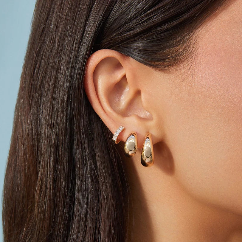 EF-Collection Prong Set Diamond Baguette Huggie Earrings in yellow gold styled on models ear with jumbo earrings