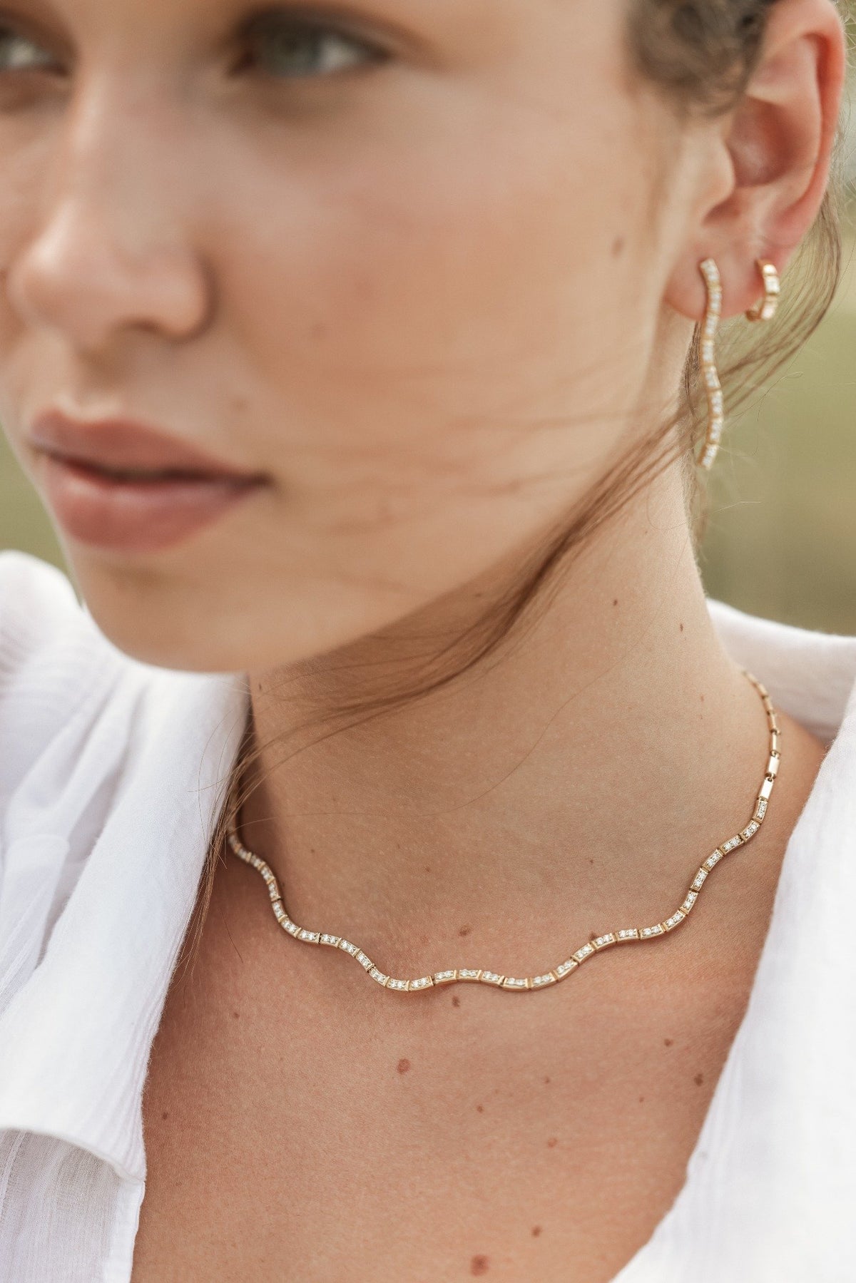 Close up of model wearing Onirikka wave necklace and wave stilleto drop earrings in yellow gold with diamonds.