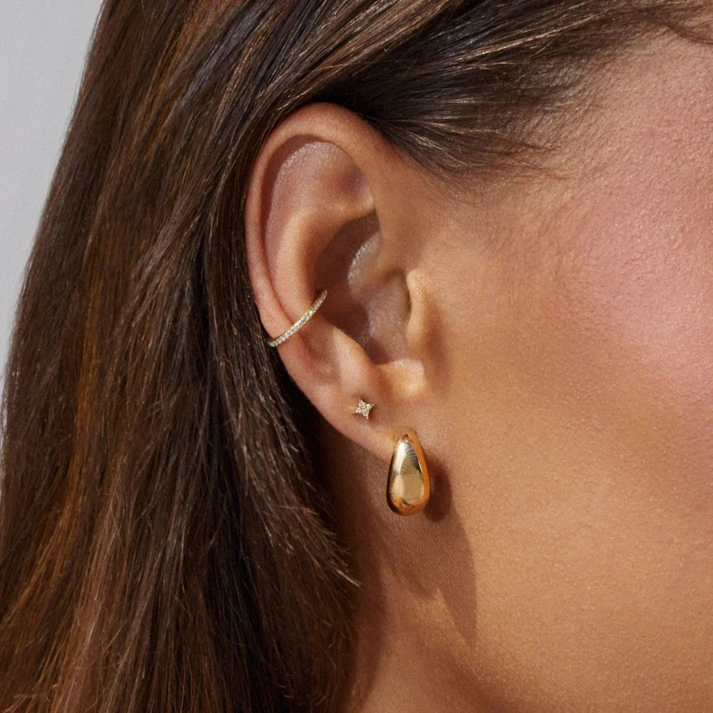 EF-Collection The Gold Jumbo Dome Huggie Earrings in yellow gold styled on models ear with an ear cuff and a diamond stud