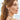 Woman with a ponytail wearing a colorful beaded necklace against a blurred background