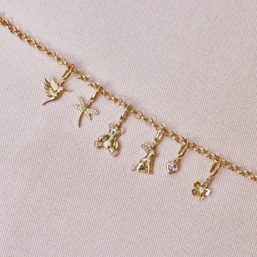 close-up of EF-Collection Gold Hummingbird Clip Charm in rose gold clipped onto a necklace chain on a baby pink background. 