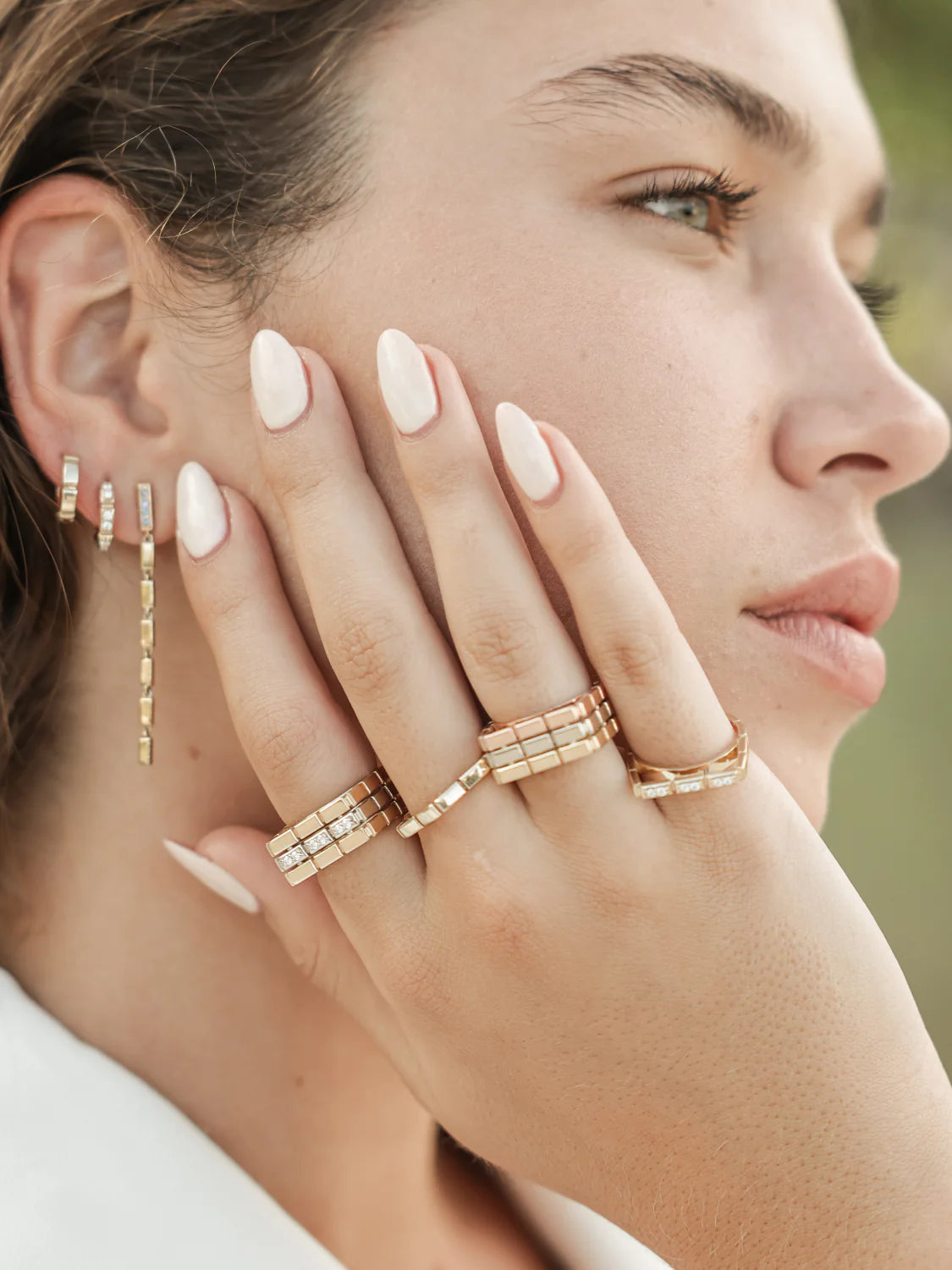 Close-up of a woman's hand wearing multiple Onirikka gold rings and diamonds with a blurred natural background