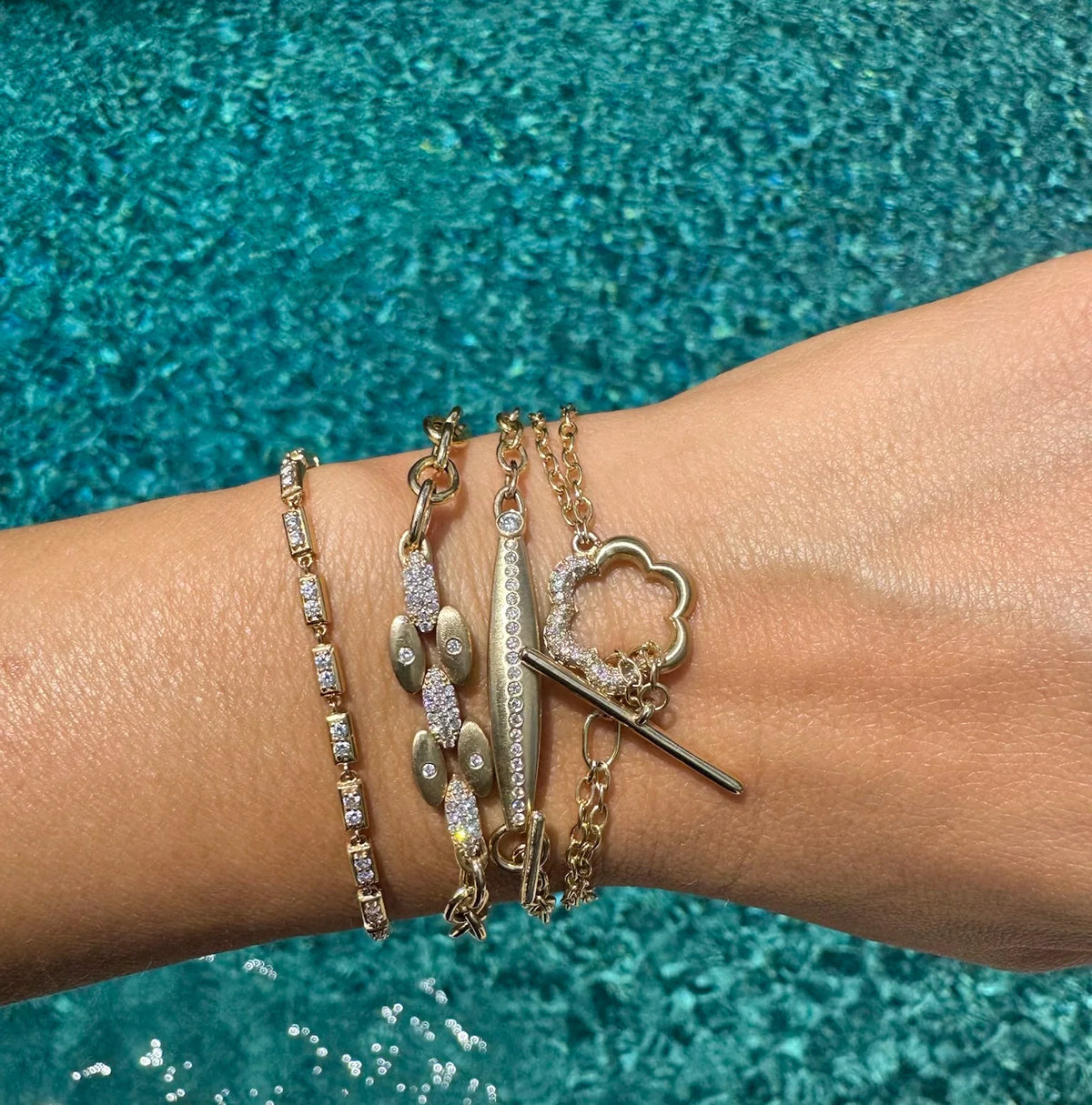 Wrist with multiple Onirikka gold bracelets against a blue glittery background.