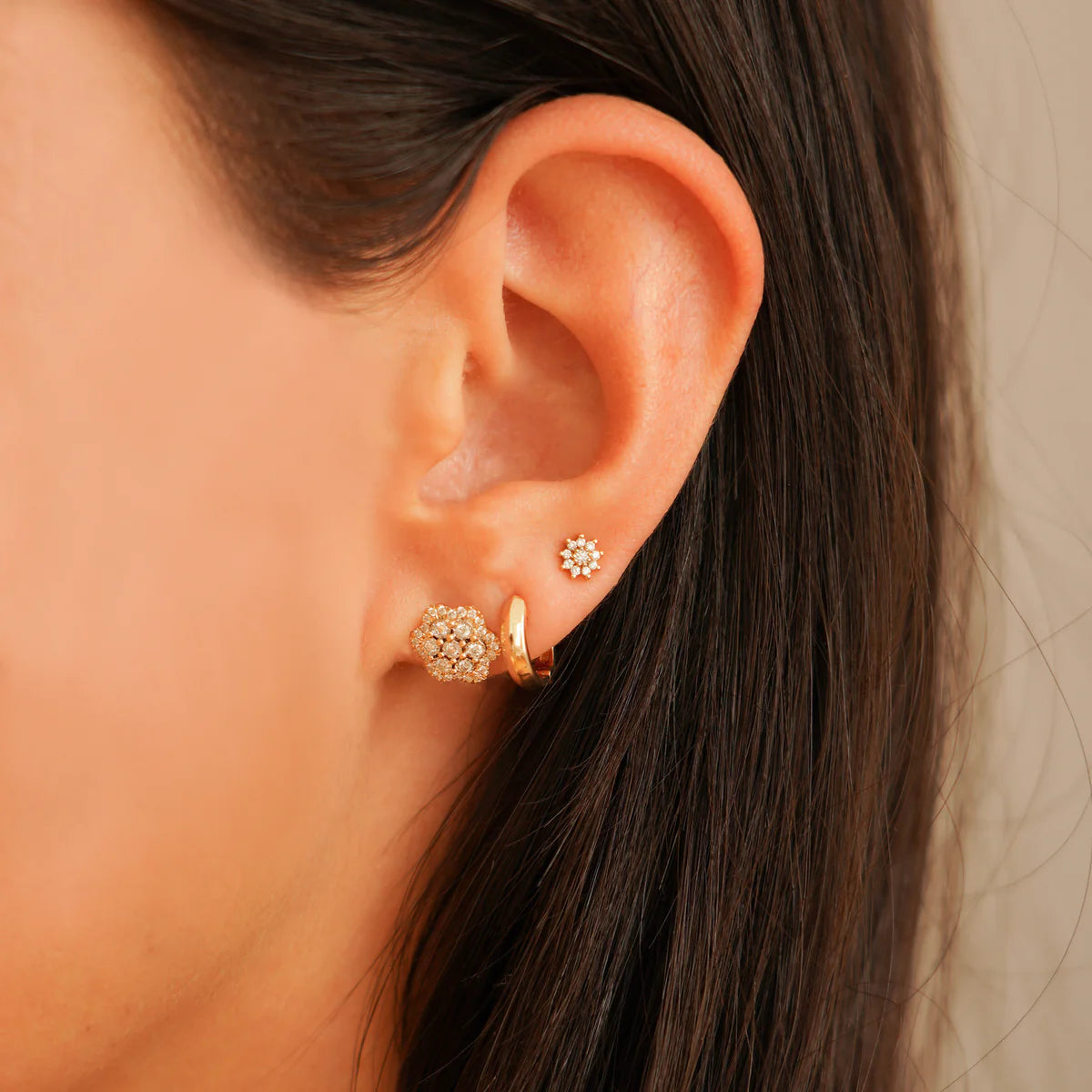 close up of Ava Bea Flower Studs in rose Gold styled on an ear with other huggies
