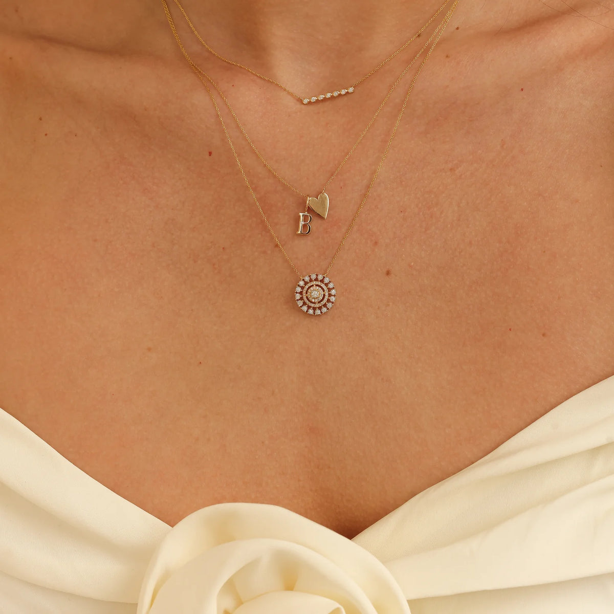 Dana Rebecca Designs Ava Bea Medallion Necklace in yellow gold on models neck layered with gold initial charm and gold heart necklace 
