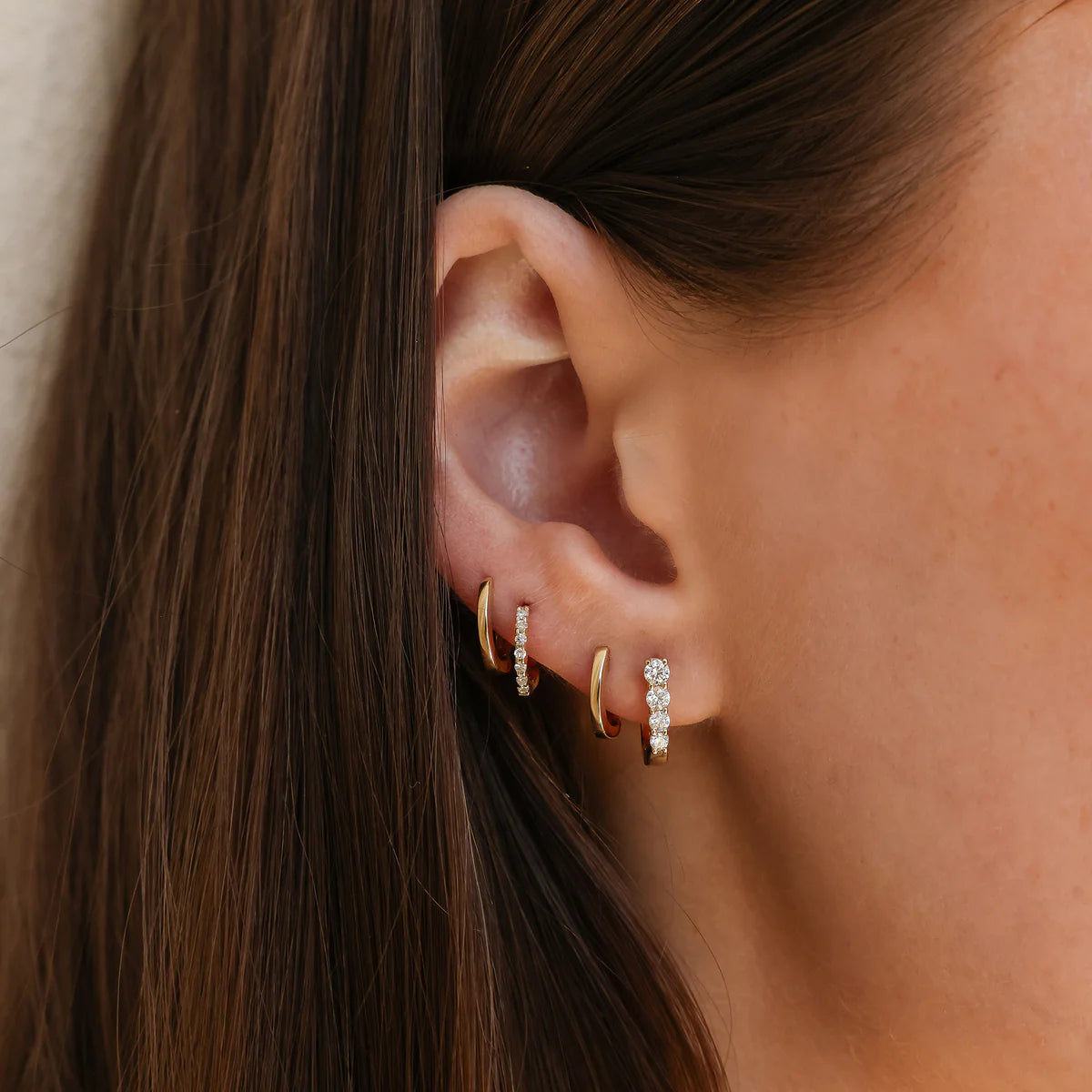 close up of Ava Bea Mini Graduating Hoop in yellow Gold styled on ear with other huggie