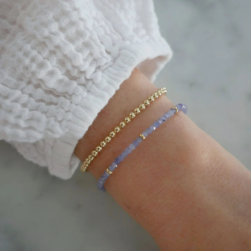EF-Collection Birthstone Bead Bracelet In Tanzanite in yellow gold styled on models wrist with yellow gold bead bracelet 