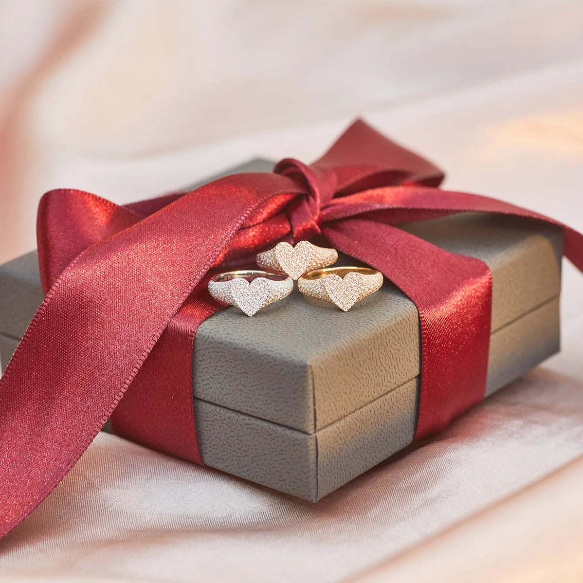 Product shot of EF-Collection Diamond Heart Signet Ring in yellow, white, and rose gold on top of a gift box with a red ribbon 