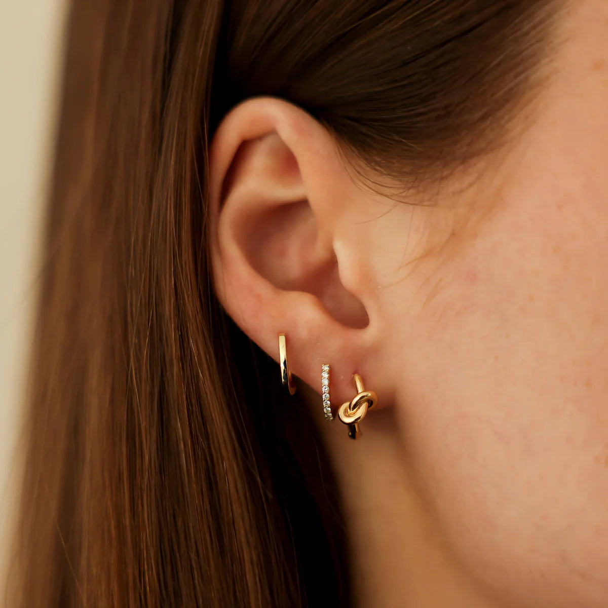 closeup of dana rebecca designs yellow gold diamond mini huggie staked in an ear