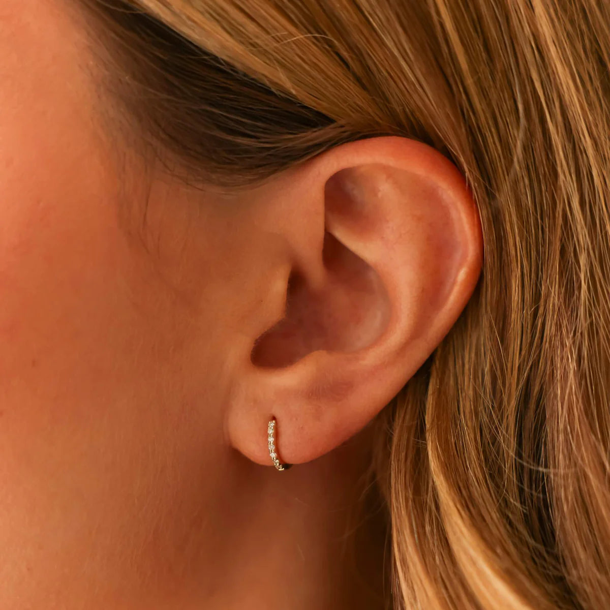 close up of ear wearing drd diamond mini huggie in yellow gold