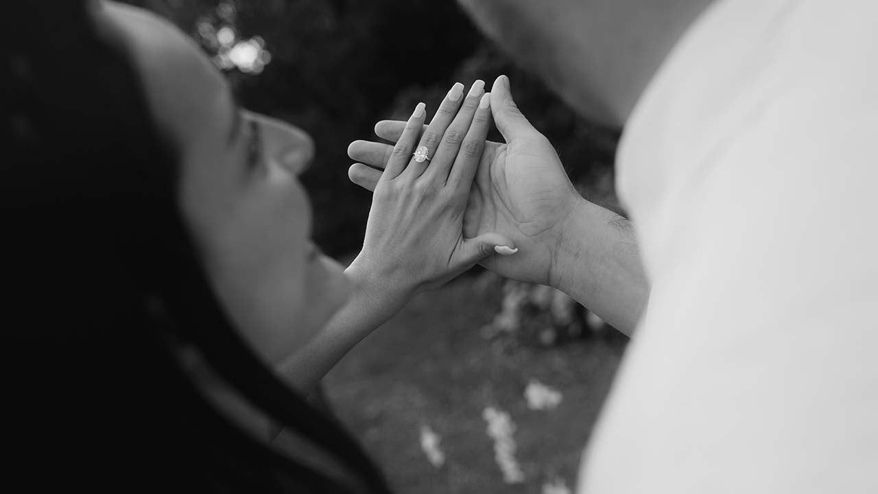 Two people holding hands and looking at their engagement ring in gold and platinum with a blurred background