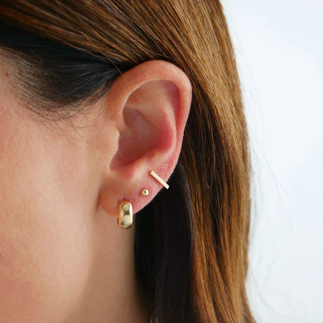 EF Collection Gold Bubble Huggie Earrings in yellow gold styled on models ear with a gold bar and a gold stud. 