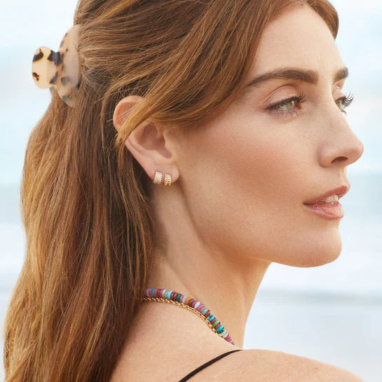 EF-Collection Gold Herringbone Mini Huggies in yellow gold styled on models ear with a blurred background 