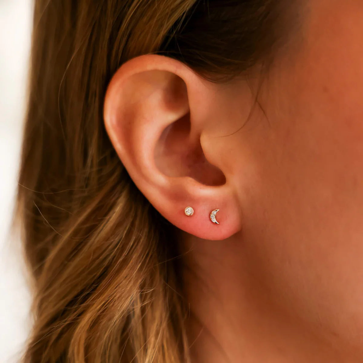 close up of Dana Rebecca Designs mini crescent moon stud earrings in yellow gold on an ear