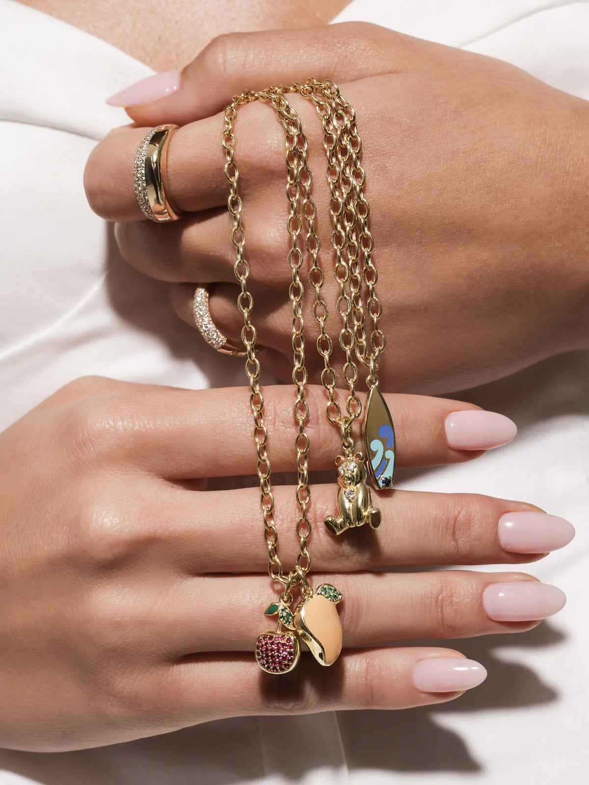 CLOSE UP OF hands holding Onirikka Gold chain necklacs with colorful enamel charms.