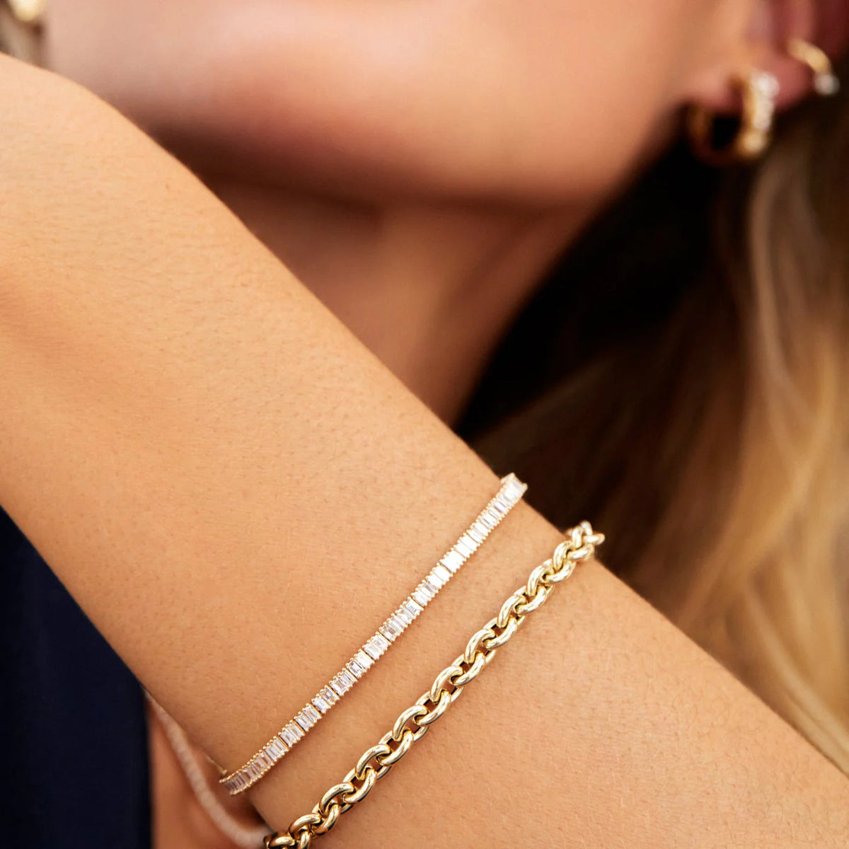 EF Collection Prong Set Diamond Baguette Eternity Bracelet in yellow gold on models wrist with yellow gold chain bracelet. 