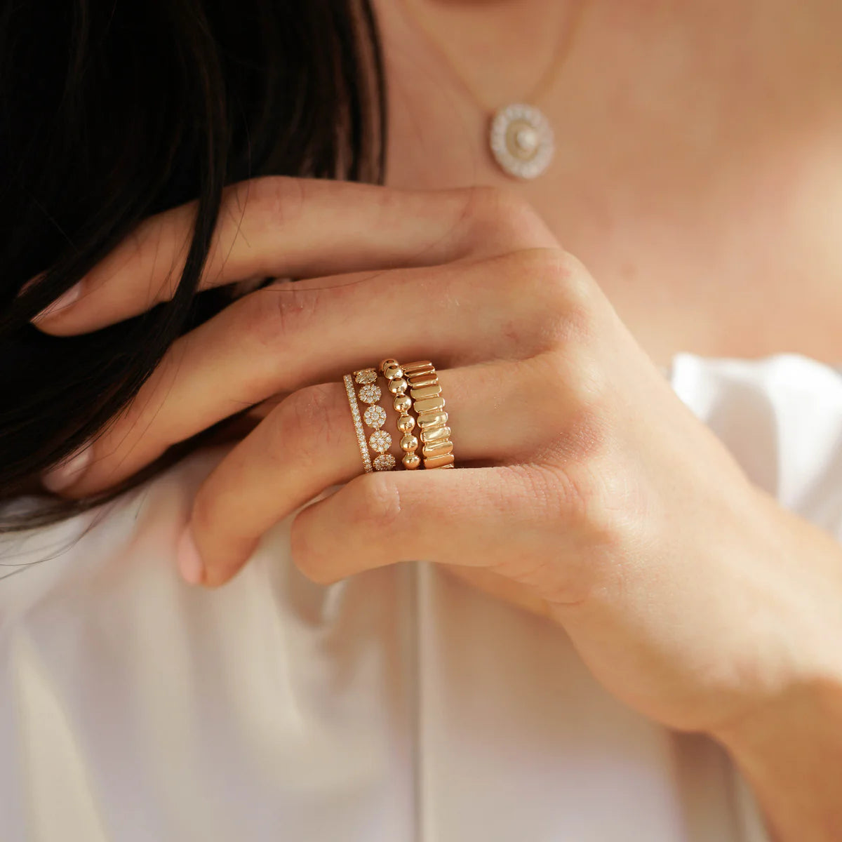 Close-up of a hand wearing Dana Rebecca Designs gold rings with a soft background