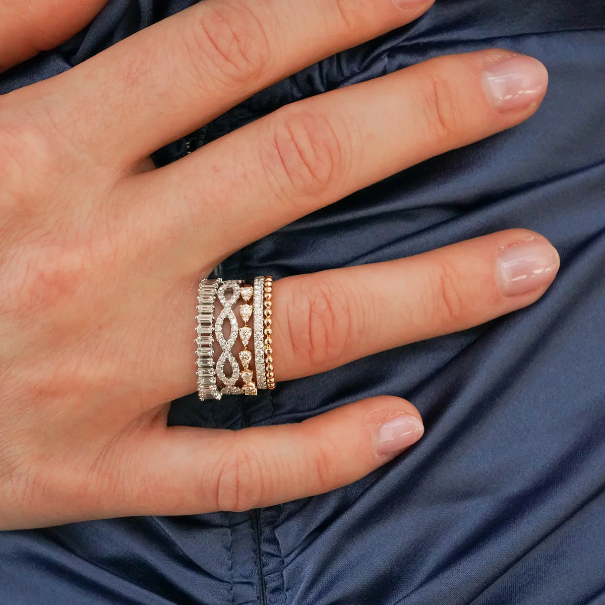 Hand wearing multiple Dana Rebecca Desings rings on a blue fabric background
