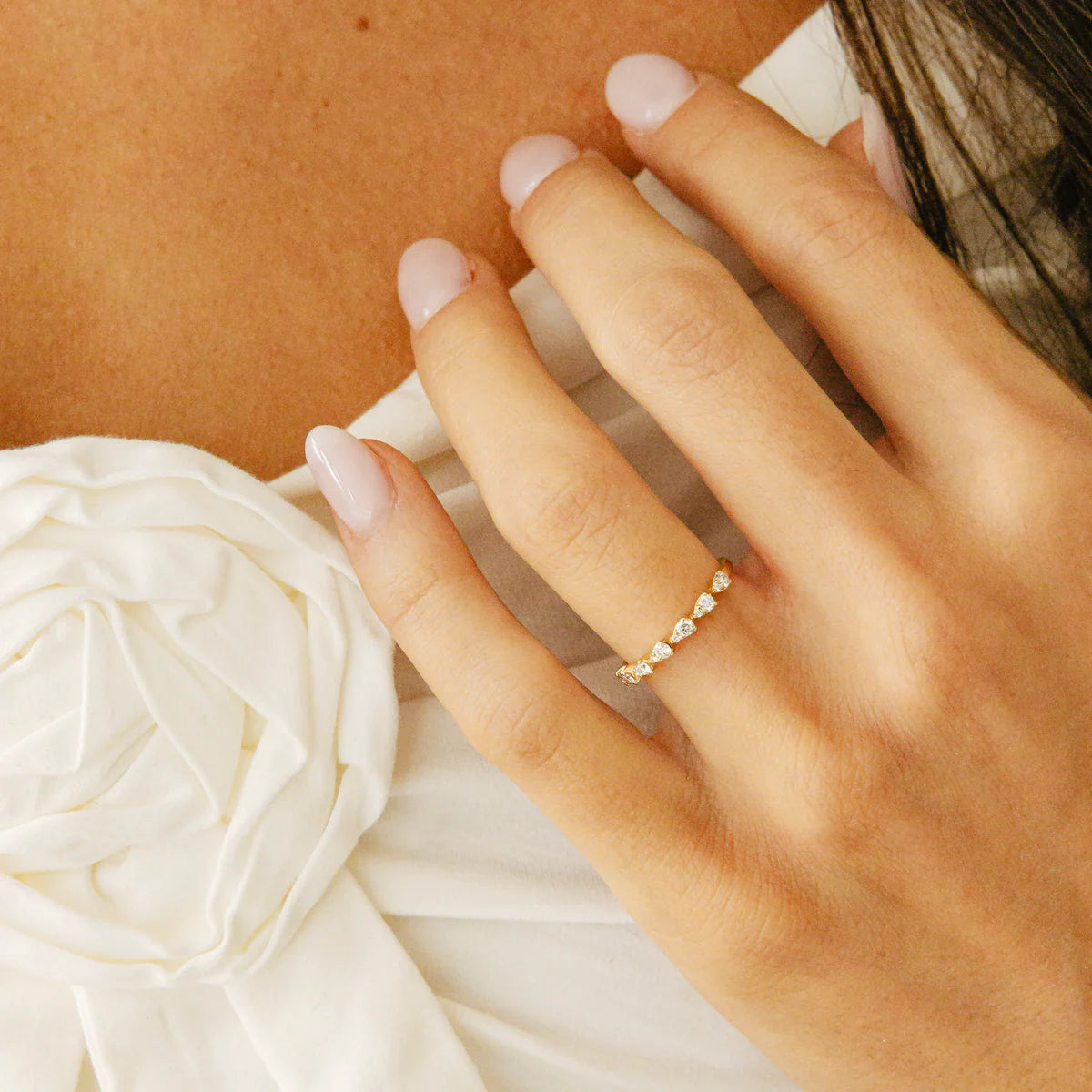 Hand wearing a Dana Rebecca Designs gold ring with a white flower in the background