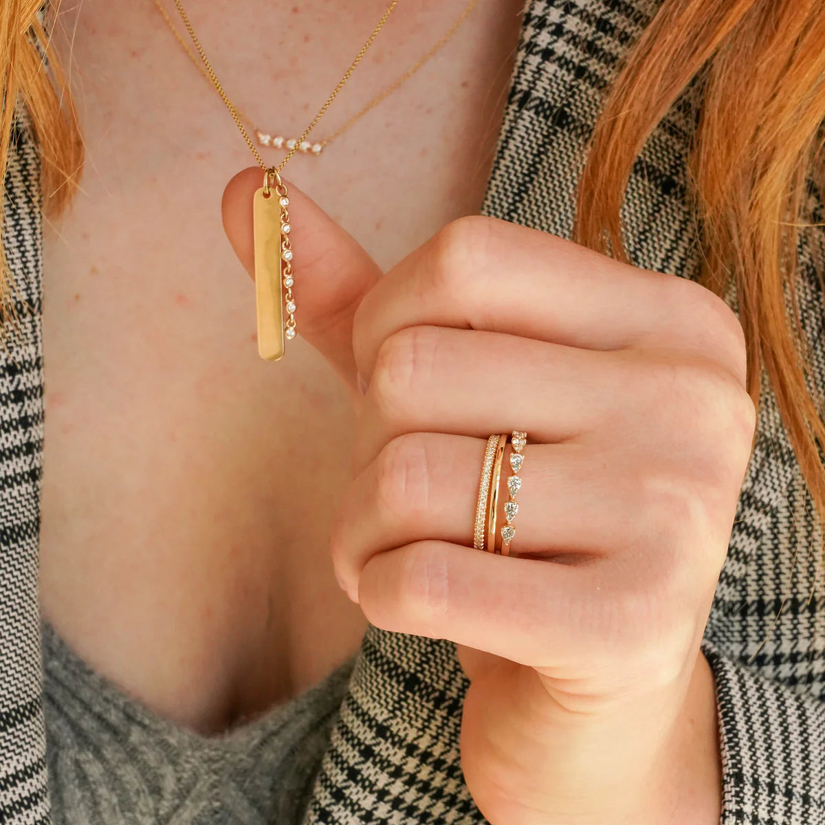 Close-up of a person wearing Dana Rebecca Designs gold necklaces and rings with a plaid garment.