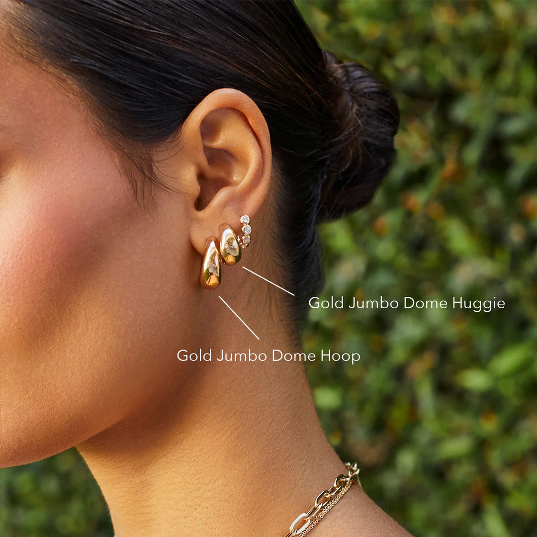 EF-Collection The Gold Jumbo Dome Huggie Earrings in yellow gold on models ear with labels 